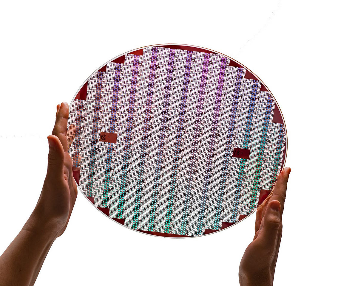 Hands holding up a large silicon wafer against a white background.