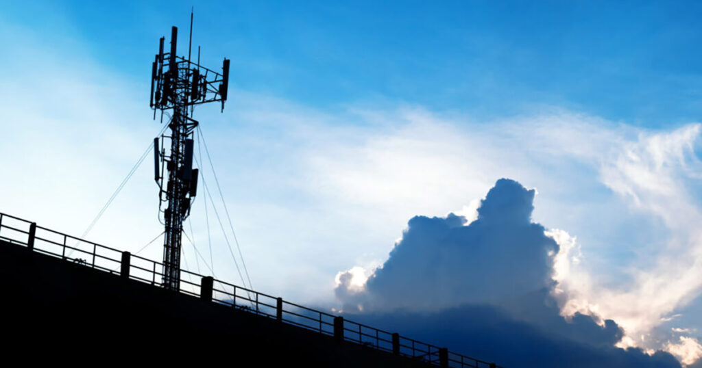 Silhouette of a cellular tower against a vibrant sunset sky with clouds.