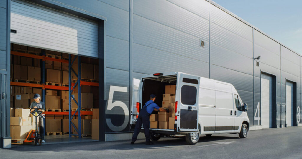 Delivery worker loading boxes into a white van at warehouse dock.