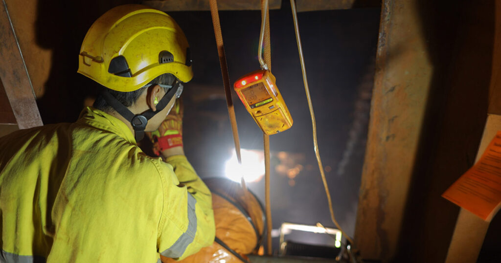 Industrial worker in yellow helmet observing readings on a handheld device.