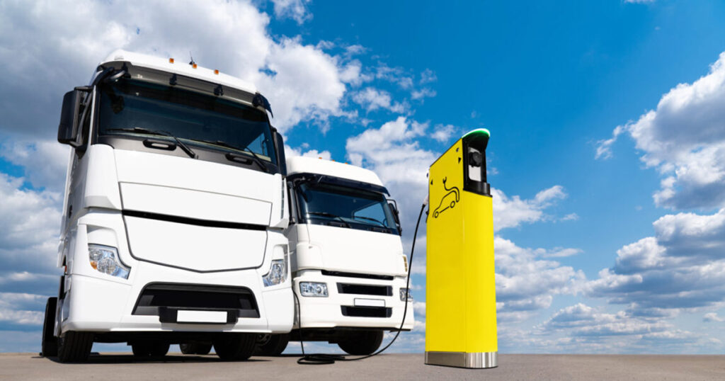 Electric truck plugged into a charging station under a cloudy sky.