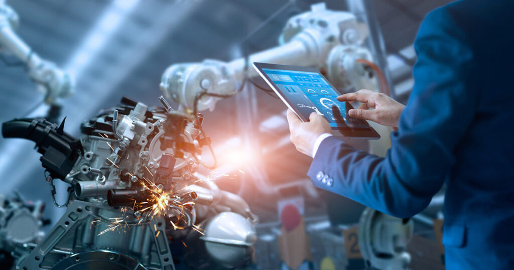 Engineer using tablet to control robotic arm in a manufacturing plant.