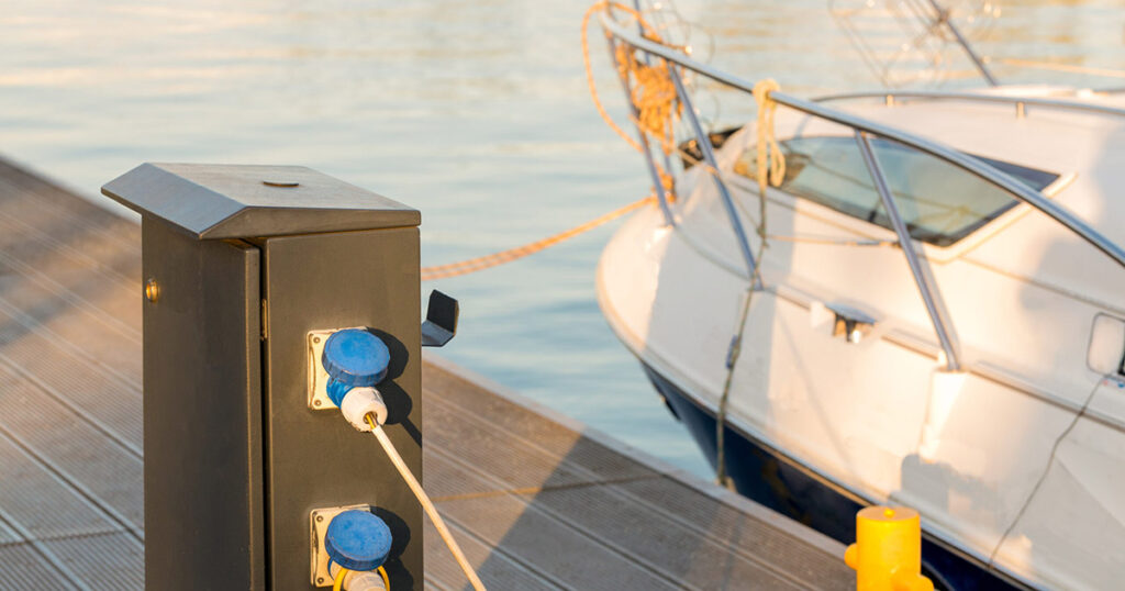 Power pedestal at a marina dock with a moored boat in the background at sunset.