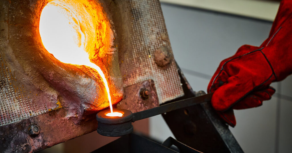 Worker pouring molten metal during a casting process in a workshop.