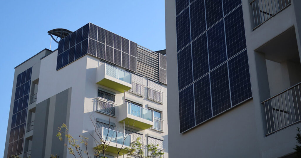 Modern building with solar panels on facade and rooftop under blue sky