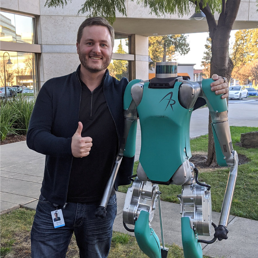 Man posing with a humanoid robot outdoors.