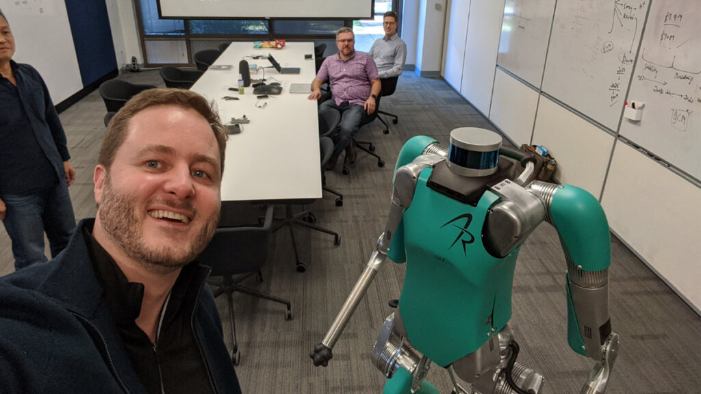 Man takes selfie with a humanoid robot in office.