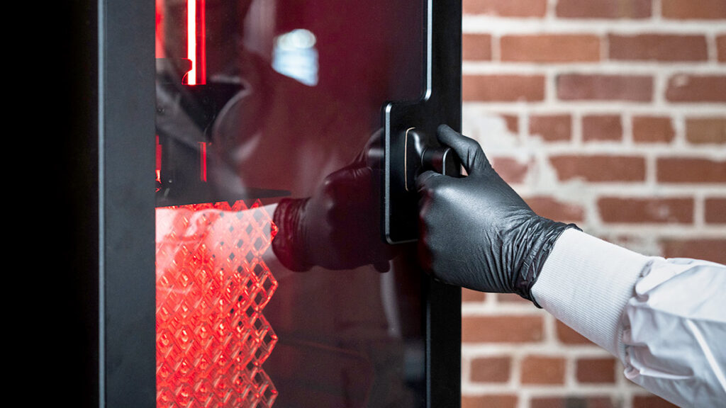 Person opening a 3D printer with red lights.