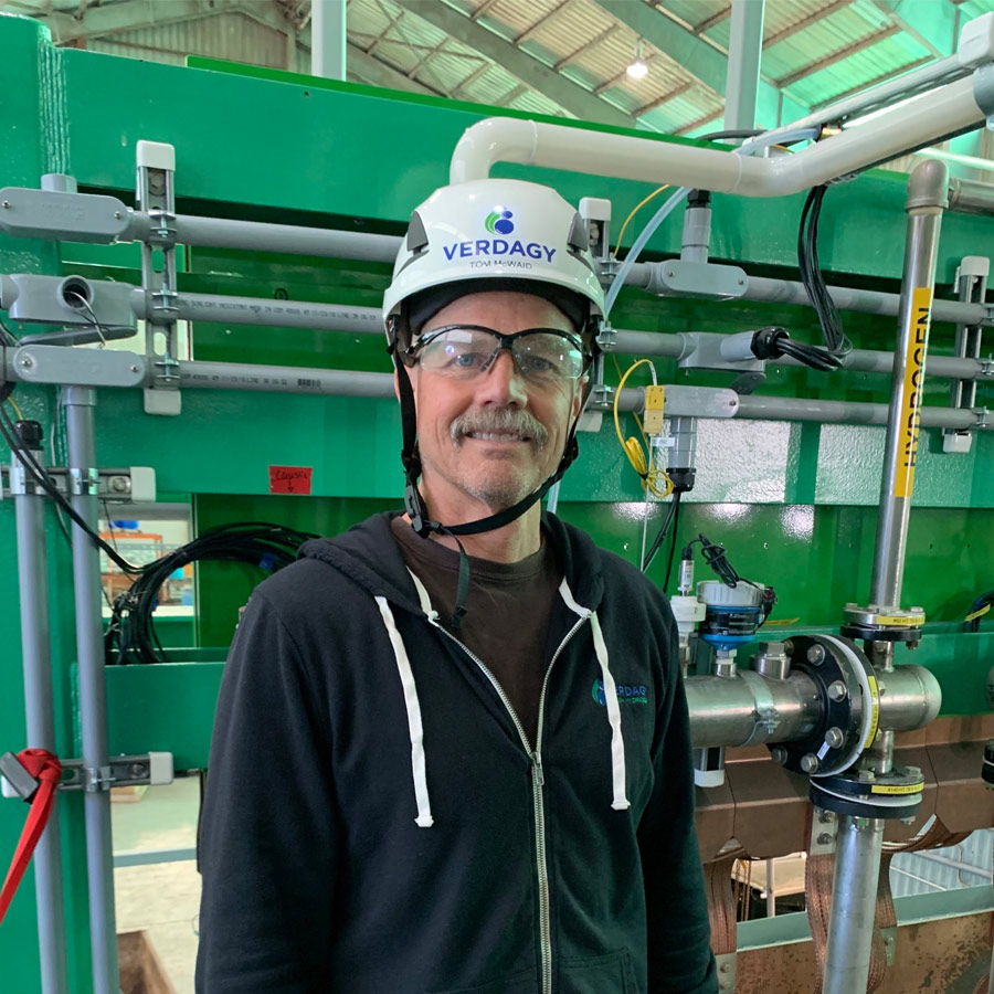 Man in hardhat smiling at industrial site.