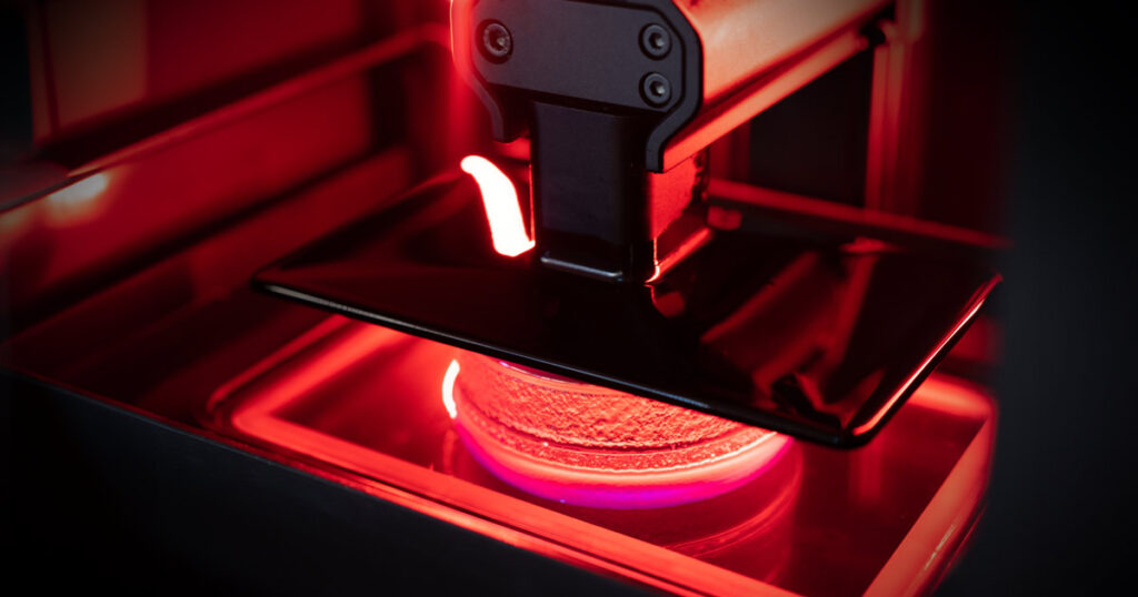 Close-up of an Origin One 3D printer creating an object with glowing red light.