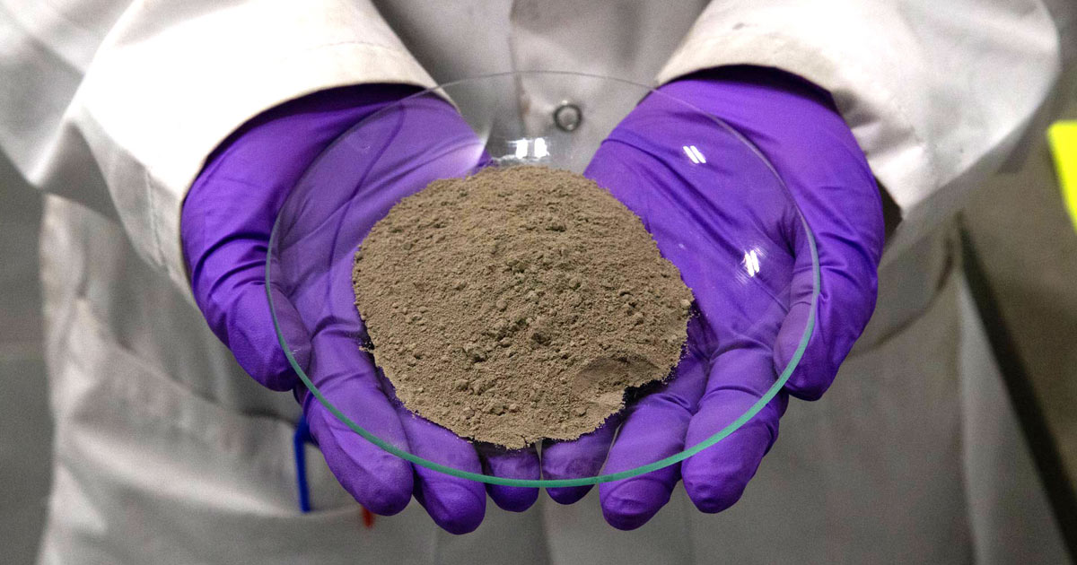 pH7 Technologies researcher in purple gloves holding a sample of refined metal powder in a lab.