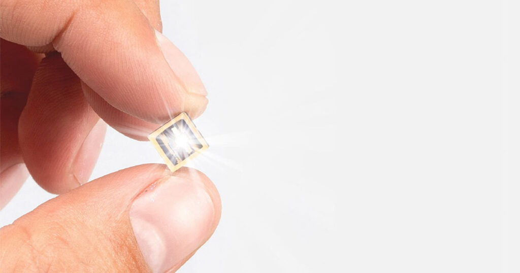 Close-up of a person holding a small SLD Laser microchip between their fingers.