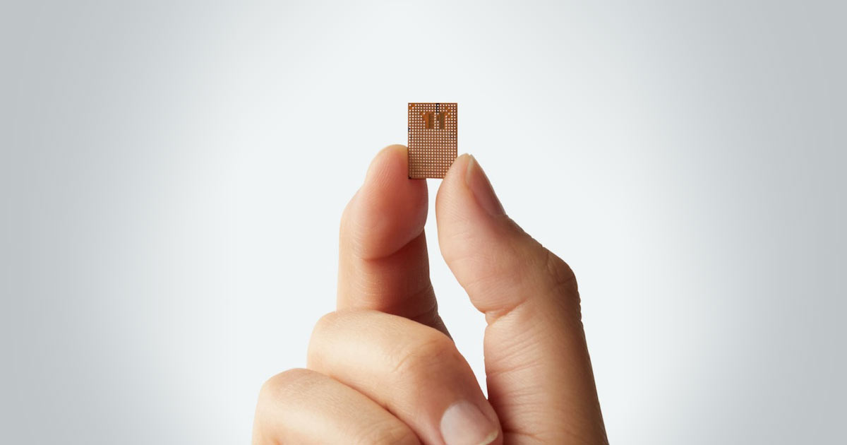 Fingers holding a small Uhnder electronic chip against a white background.