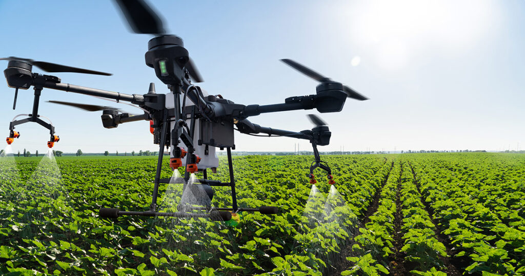 Drone applying pesticides over a green crop field on a sunny day.