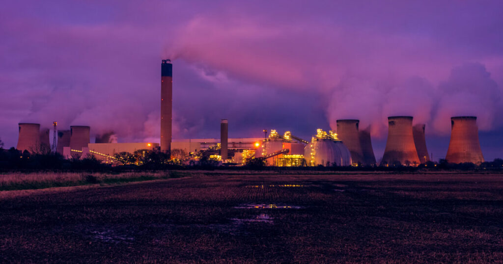 Twilight view of industrial power plant with smokestacks and cooling towers.