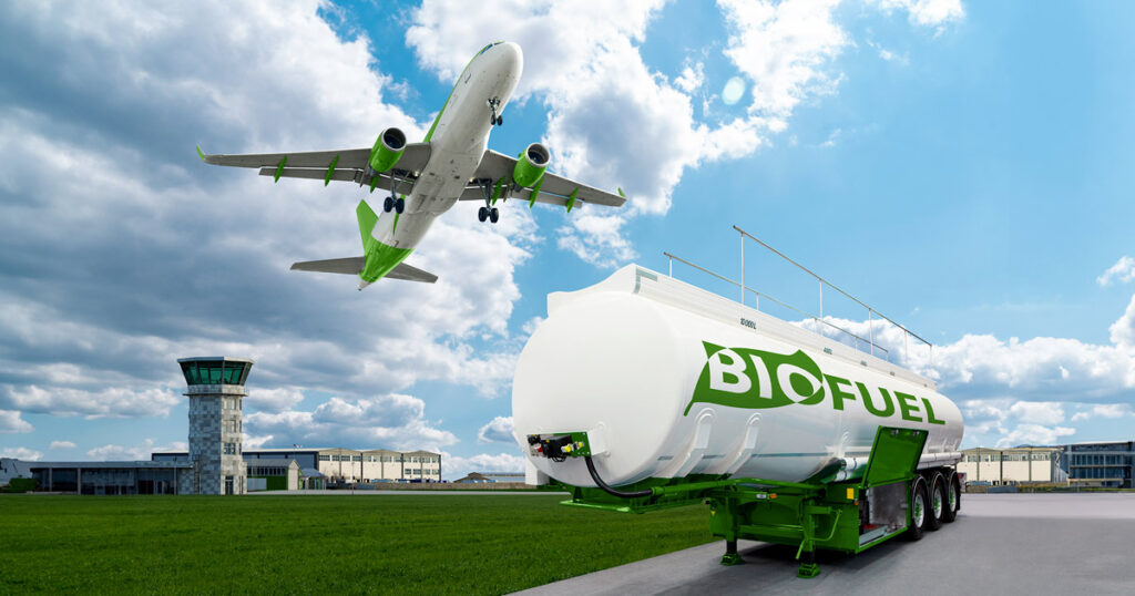 Airplane landing near a biofuel tanker at an airport with control tower in the background.