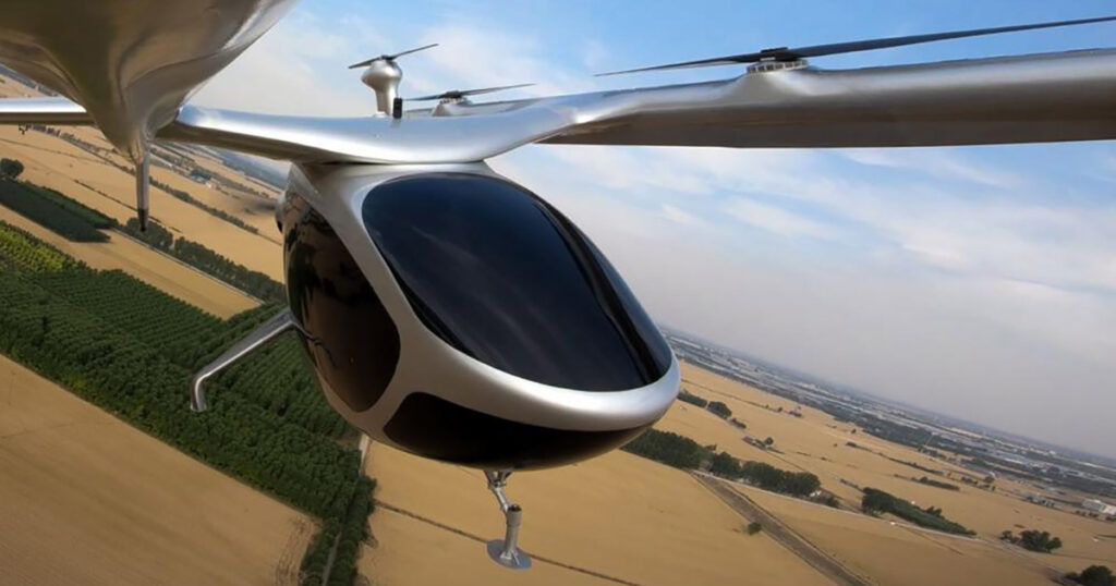 Electric aircraft flying over farmland with clear skies.