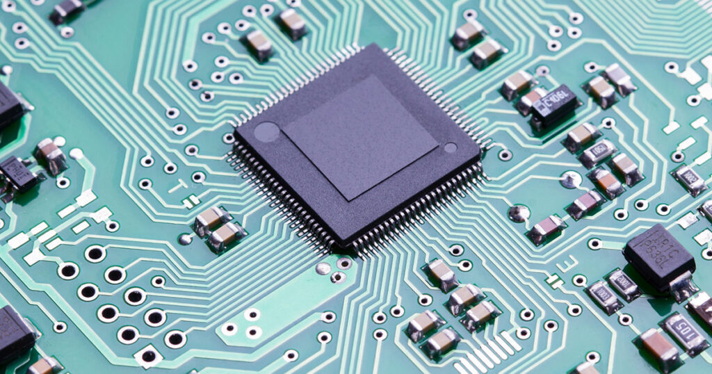 Close-up of a microchip on a green circuit board with various electronic components.