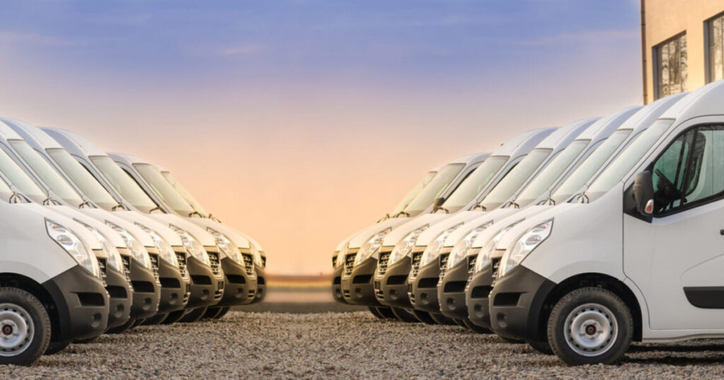 Line of white delivery vans parked side by side during sunset.