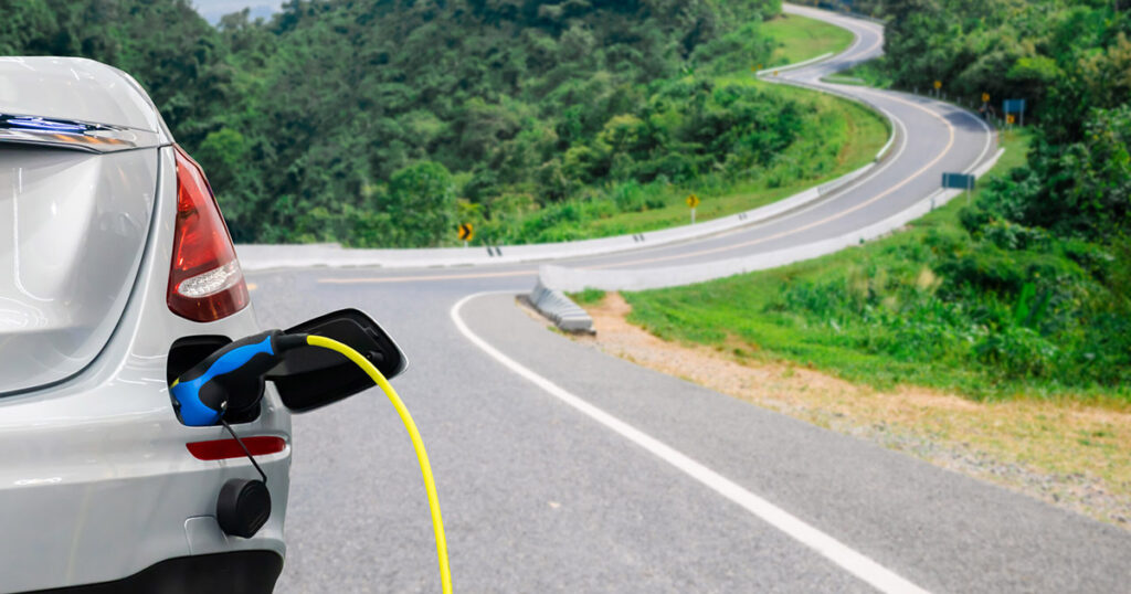 Electric vehicle charging with scenic winding road in background.