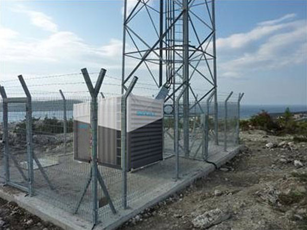 Cell tower secured by a fence on a hill.