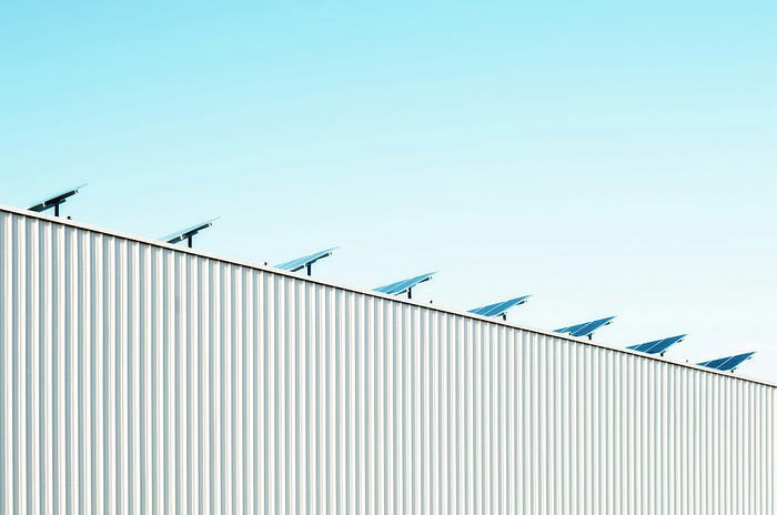 Solar panels on a corrugated metal roof against a clear blue sky.