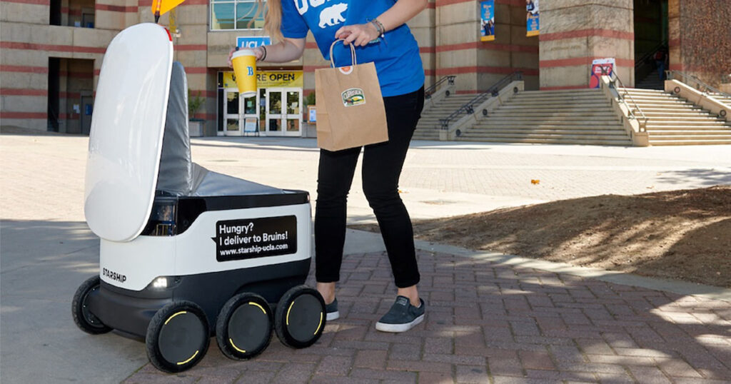 A Starship delivery robot on a university campus providing service to a person.