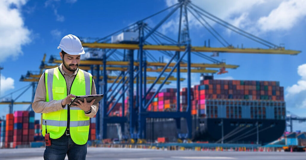 Engineer with tablet inspecting cargo at a busy shipping dock.